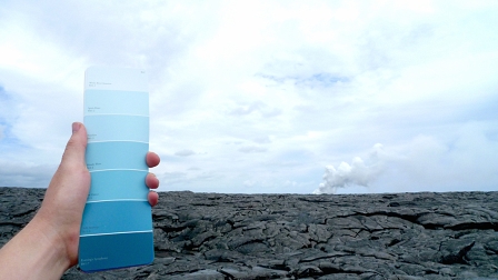 Hand hält eine Farbskala Richtung Himmel. Im Hintergrund Lava-Boden.